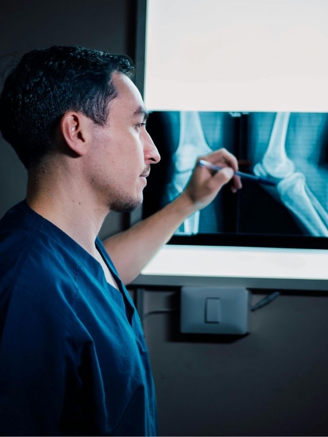 Ortopedico che analizza una radiografia del ginocchio con il paziente durante una visita medica.